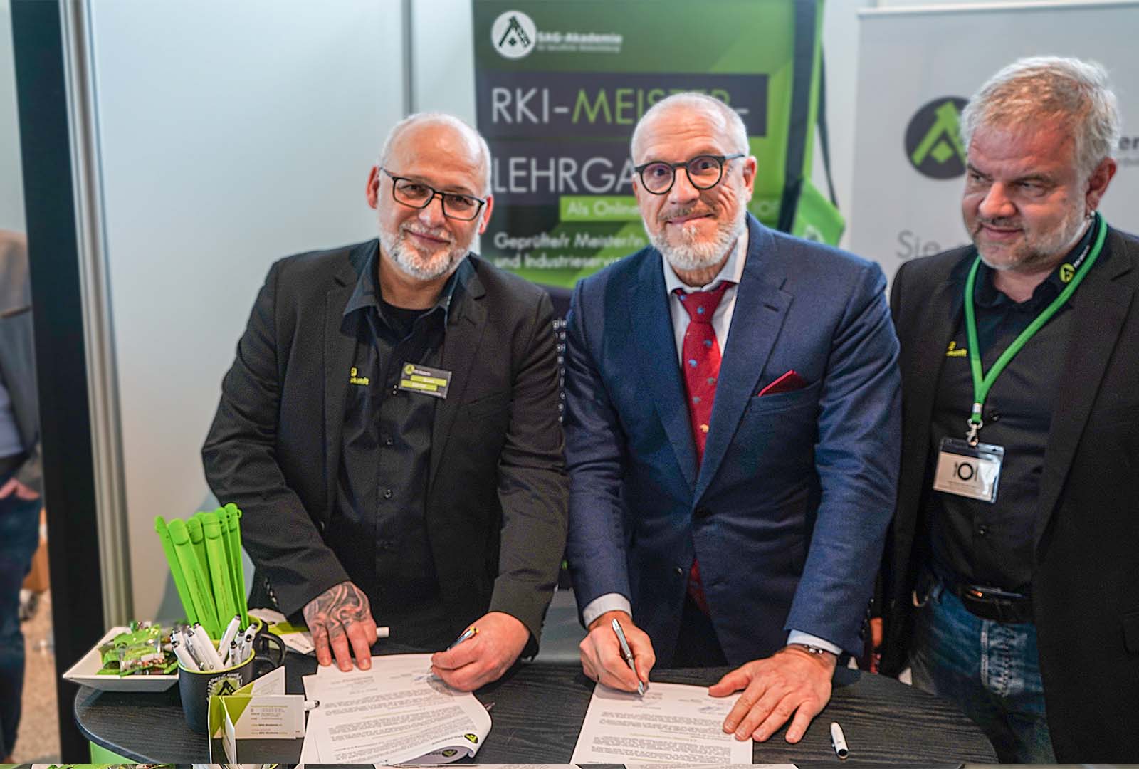 Three men signing documents at a conference booth.